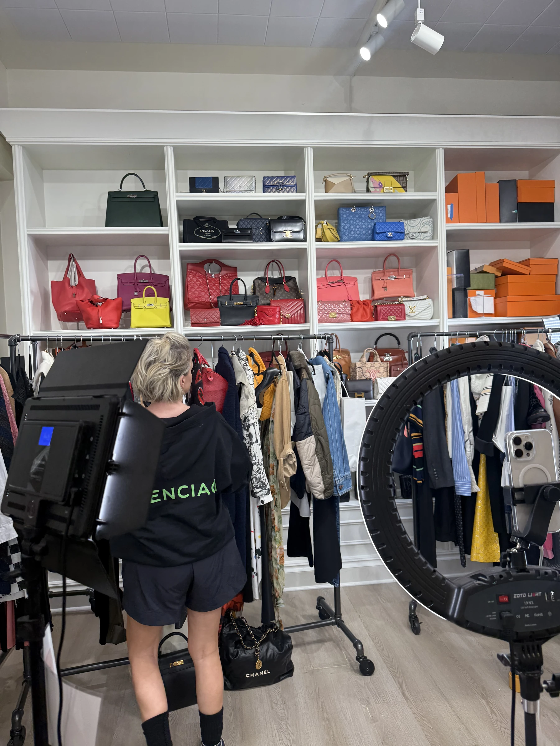 Behind-the-scenes livestream setup with clothing racks, product displays, and a ring light.